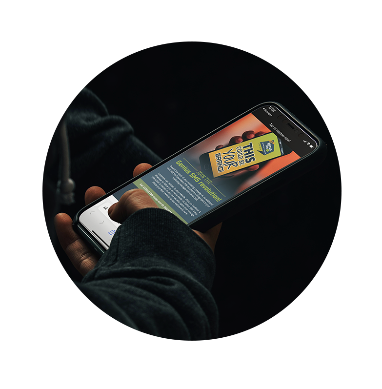 A hand holding a smartphone viewing a Genius SMS flyer and using the thumb to tap on a link within the digital flyer.